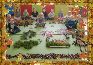 Na zdjęciu grupa dzieci. Przed nimi jesienna kopozycja z naturalnych materiałów.
